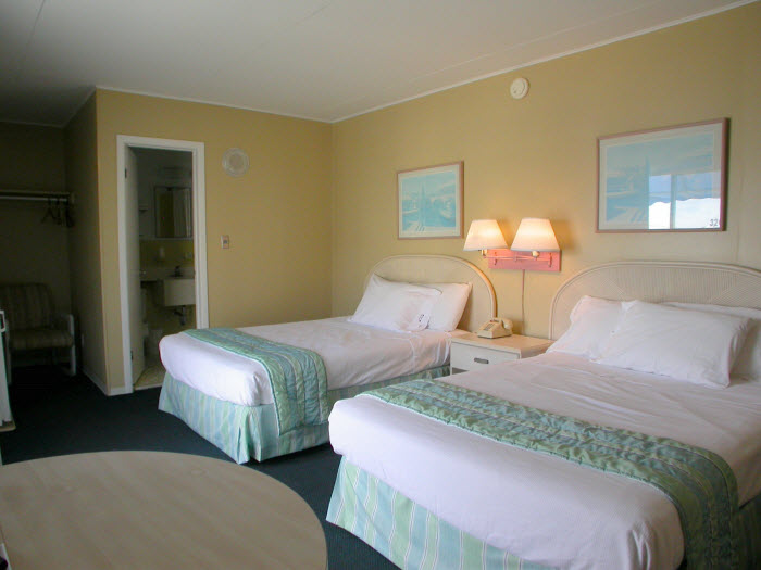 A hotel room with two twin beds, a nightstand, and a doorway to the bathroom.