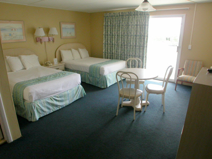 A hotel room with two beds, a table and chairs, and a door leading outside.