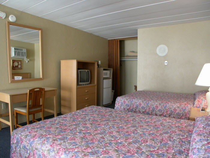 A hotel room with two beds, a desk, a TV, and a small fridge.
