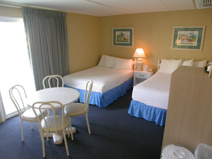 A hotel room with two beds, a table, chairs, and a window.