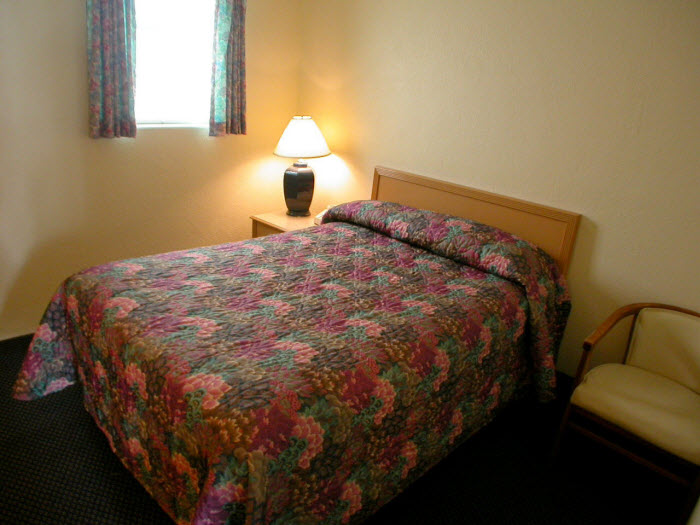 A hotel room with a bed, lamp, chair, and window.
